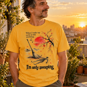 I'm Only Sweeping AP21 graphic T-shirt featuring a Japanese ink-style broom, human-shaped dust silhouette, red sun, cherry blossoms and musical notes on a cream background.